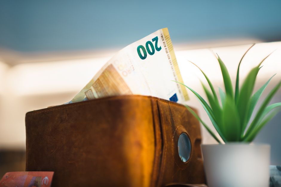 Empty wallet beside growing stack of saved banknotes